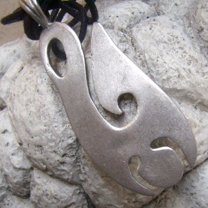 May include: A silver pendant with a stylized, abstract design. The pendant has a smooth, polished finish and features a series of cutouts.