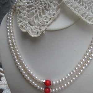May include: A double strand pearl necklace with two red coral beads and small clear rhinestones.