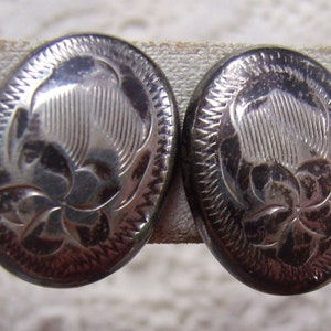 May include: A pair of silver oval-shaped earrings with a floral design. The earrings have a textured border.