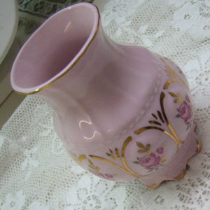 May include: A pink porcelain vase with gold accents and a floral design. The vase has a wide mouth and a rounded body.