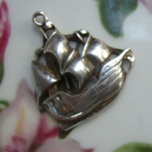May include: A silver charm in the shape of a sailing ship. The ship has a detailed design with a raised sail and a textured hull.
