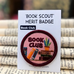 Puede incluir: Un parche bordado de color rosa y marrón con el texto "BOOK CLUB" y una pila de libros y una planta en maceta. El parche está etiquetado como "Book Scout Merit Badge" y "Book Club".