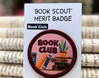 May include: A pink and maroon embroidered patch with the text "BOOK CLUB" and a stack of books and a potted plant. The patch is labeled "Book Scout Merit Badge" and "Book Club".