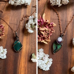 Könnte beinhalten: Zwei Halsketten aus Kupferdraht mit Edelsteinanhängern. Die erste Halskette hat einen Anhänger aus grünem Stein. Die zweite Halskette hat einen Anhänger aus grünem und violettem Stein.