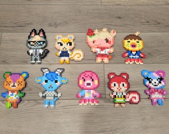 Può includere: Dieci personaggi di pixel art colorati della serie di videogiochi Animal Crossing. I personaggi sono fatti di piccole perline di plastica e sono disposti su due file su una superficie di legno.