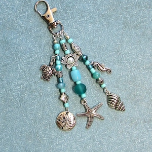 May include: A silver key chain with blue and silver beads, charms, and a starfish. The charms include a turtle, a seashell, and a flower.