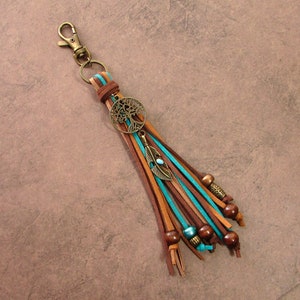May include: A brown leather keychain with a turquoise and brown tassel, a tree of life charm, and a small feather charm. The keychain has wooden beads and a metal clasp.