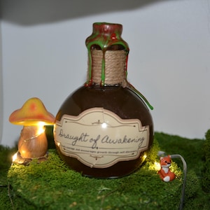 May include: A brown potion bottle with a label reading "Draught of Awakening" sits on a bed of green moss. A small, illuminated mushroom and a tiny fox figurine are nearby. The bottle's neck is wrapped with twine and sealed with red and green wax.
