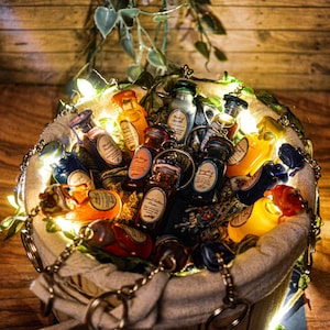 Puede incluir: Un saco de arpillera lleno de pequeñas botellas de vidrio, algunas con líquidos coloridos, otras con etiquetas. Las botellas están rodeadas de una cadena de luces blancas.