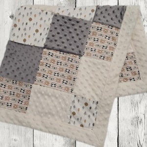 May include: A patchwork baby blanket featuring squares of various patterns and textures. The blanket includes squares with panda bear designs, gray polka dots, and a cream-colored fabric with a tree pattern. The border and backing are a soft, cream-colored minky fabric.