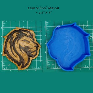 May include: A blue silicone mold of a lion head, approximately 4.5 inches by 5 inches, next to a brown and black lion head design on a cork-like material.