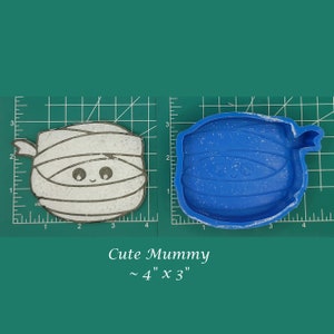 May include: A white and blue mummy-shaped silicone mold for resin crafts. The mold is approximately 4 inches by 3 inches. The mold is on a green cutting mat.