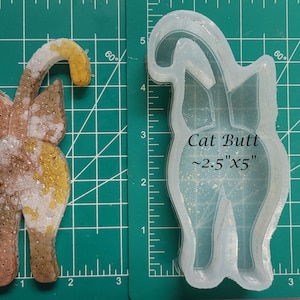 May include: A clear silicone mold for making resin crafts. The mold is shaped like a cat's rear end and is labeled "Cat Butt ~2.5"x5" ".