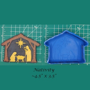 May include: A brown and blue plastic mold for making a nativity scene. The mold is approximately 4.5 inches by 3.5 inches. The mold is on a green grid background.