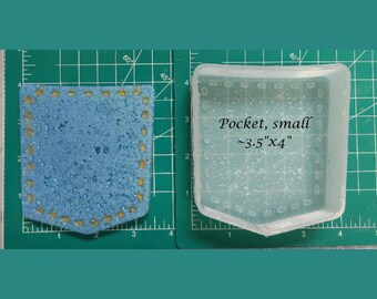Op de afbeelding: Een transparante plastic mal voor het maken van een klein zakje, ongeveer 3,5 inch bij 4 inch. De mal ligt op een groene snijmat.