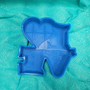 May include: Blue plastic cookie cutter shaped like a heart with a heartbeat line, the letter 'N' and a caduceus symbol.