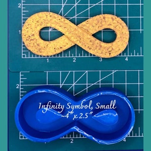 May include: A blue silicone mold shaped like an infinity symbol. The mold is on a green cutting mat with white markings. The text "Infinity Symbol, Small ~4" x 2.5"" is written on the mold.