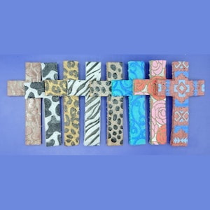 Puede incluir: Un conjunto de diez pequeñas cruces de madera con varios patrones coloridos, incluyendo estampados de animales, diseños florales y formas geométricas.