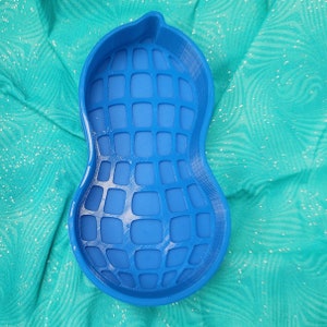 Puede incluir: Un cuenco azul en forma de cacahuete para la alimentación lenta de mascotas. El cuenco tiene una superficie texturizada con un patrón de cuadrícula.