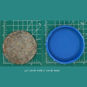 Op de afbeelding: Een cirkel van 8,9 cm met een cirkel van 7,6 cm inzet. De grotere cirkel is gemaakt van een bruin en grijs materiaal, terwijl de kleinere cirkel een blauwe plastic deksel is.
