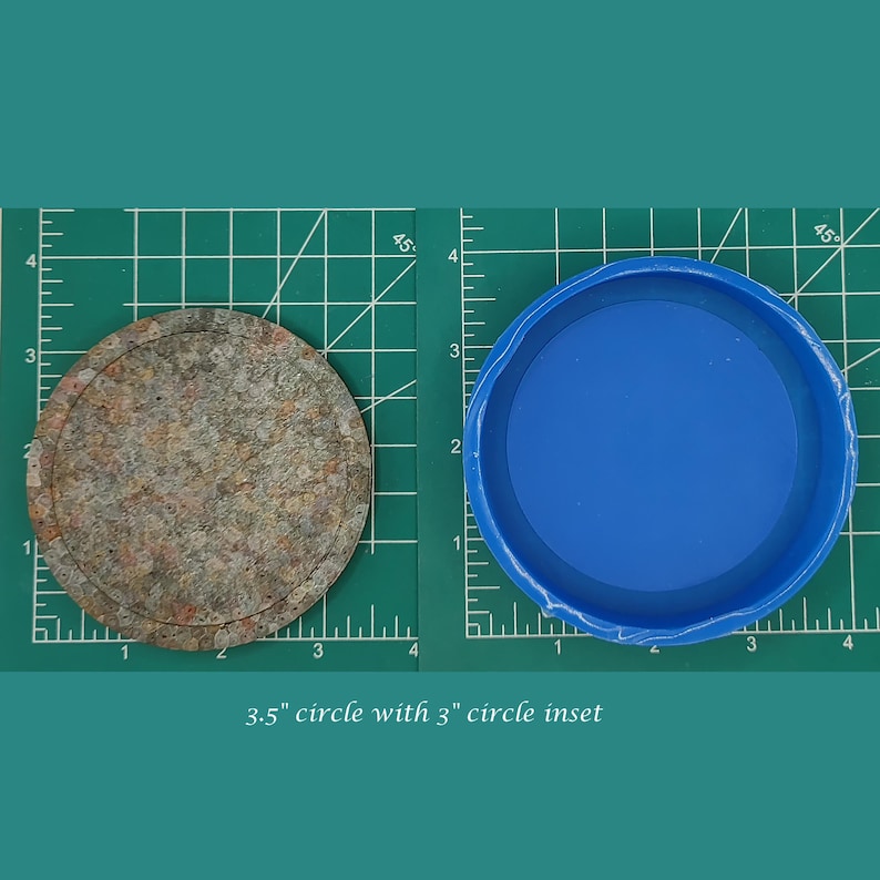 Op de afbeelding: Een cirkel van 8,9 cm met een cirkel van 7,6 cm inzet. De grotere cirkel is gemaakt van een bruin en grijs materiaal, terwijl de kleinere cirkel een blauwe plastic deksel is.
