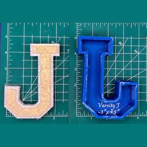 Puede incluir: Dos moldes de letras J, uno es amarillo y el otro es azul. El molde azul tiene el texto "Varsity J ~3" x 4.5"