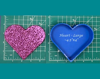 May include: A blue heart-shaped silicone mold for crafting. The mold is 4.5 inches by 4 inches and is on a green cutting mat.