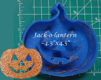 Puede incluir: Un cortador de galletas de plástico azul con forma de Jack-o-lantern junto a una calabaza naranja con purpurina. El cortador mide aproximadamente 11,4 cm x 11,4 cm y tiene la inscripción "Jack-o-lantern".