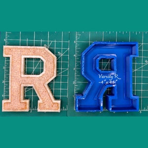 May include: Two letter R molds, one is beige and the other is blue. The blue mold has the text "Varsity R - 4" x 4.5" written on it.