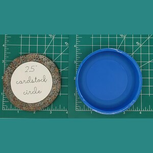 Op de afbeelding: Een cirkel van bruin karton met een diameter van 2,5 inch met een witte cirkel in het midden. De witte cirkel heeft de tekst "2,5" cardstock circle" erop geschreven. De cirkel van karton ligt naast een blauwe plastic cirkel van dezelfde grootte.