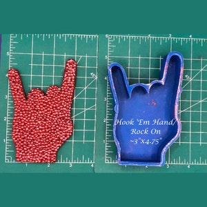 May include: Blue silicone mold of a hand making the rock on hand gesture. The mold is 3 inches by 4.75 inches and says "Hook 'Em Hand/Rock On" on the inside.