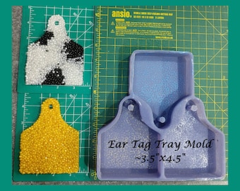 May include: Purple silicone mould for making ear tags. The mould is shaped like an ear tag and is approximately 3.5 inches by 4.5 inches. The mould is on a green cutting mat.