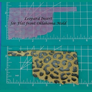 May include: Leopard print insert for a flat front Oklahoma state mould. The insert is approximately 15 cm wide and 10 cm tall. The insert is on a green cutting mat with a ruler.