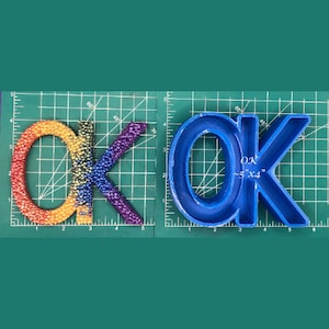 May include: Two "OK" letters, one made of rainbow colored beads and the other a blue plastic mold. The mold is approximately 5 inches by 4 inches.