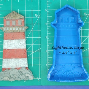 May include: A blue silicone mold of a lighthouse with a white base and red stripes. The mold is approximately 2.5 inches wide and 5 inches tall. The mold is on a green cutting mat with white markings.