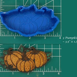 Puede incluir: Molde de silicona azul para hornear tres calabazas. El molde mide 3,5 pulgadas por 1,75 pulgadas. El molde se muestra junto a un conjunto de tres calabazas horneadas en el molde.