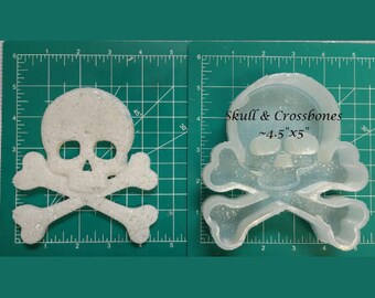 Puede incluir: Un molde de silicona transparente de una calavera y huesos cruzados. El molde mide aproximadamente 11,4 cm por 12,7 cm.