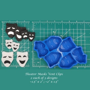 May include: A blue silicone mold for making theater mask-shaped vent clips. The mold has six cavities, each shaped like a different theater mask. The mold is shown next to six finished vent clips, two of each design, in black and white foam. The text "Theater Masks Vent Clips, 2 each of 3 designs, ~1.5" X 2"; ~2" X 1.5" is printed below the mold.