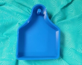 May include: A blue plastic mould shaped like a cow tag. The mould has a hole at the top for hanging.