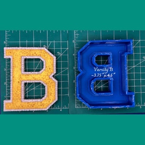 May include: A yellow and white foam letter B with a blue plastic mold of the same letter. The mold is labeled "Varsity B ~3.75" x 4.5" "