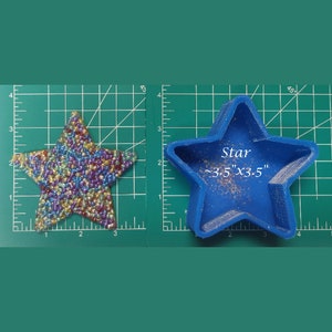 Puede incluir: Un objeto en forma de estrella con una superficie texturizada e iridiscente junto a un molde azul en forma de estrella. El molde azul está etiquetado "Star ~8.9cm x 8.9cm" sobre un fondo de cuadrícula verde.