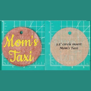 May include: A 3.5 inch round wooden sign with the words "Mom's Taxi" written in yellow paint. The sign is on a green cutting mat.