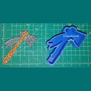 May include: A blue plastic mould of a tomahawk with the text "Tomahawk ~4"X4" on the mould. The mould is on a green cutting mat with white markings.