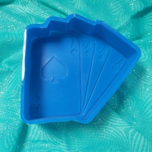 Puede incluir: Molde de silicona azul con forma de cuatro cartas de juego, cada carta tiene un as y un símbolo de picas.