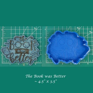 Puede incluir: Un molde de silicona azul para fundición de resina. El molde tiene la forma de las palabras "The Book was Better". El molde mide aproximadamente 4,5 pulgadas por 3,5 pulgadas.