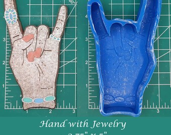 Op de afbeelding: Een blauwe siliconen mal van een hand die de rock-and-roll handgebaar maakt. De mal is 2,75 inch bij 5 inch. De hand draagt ​​sieraden.