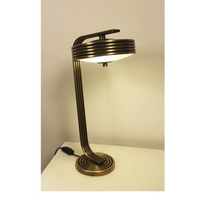 May include: A brass desk lamp with a curved, multi-layered stem and a round, white glass shade.