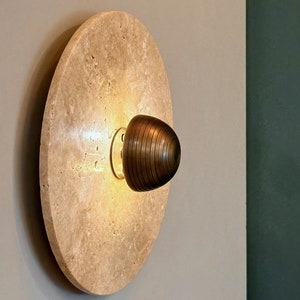 May include: A round, beige stone wall sconce with a light bulb and a brown, ribbed glass shade.