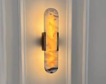 May include: A white and brown marble wall sconce with a brass frame. The sconce is illuminated with a warm white light.