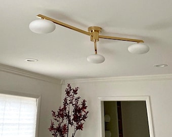 May include: A modern ceiling light fixture with a gold finish and three frosted glass globe shades. The fixture is mounted on a white ceiling and has a minimalist design. The light fixture is a stylish addition to any room.